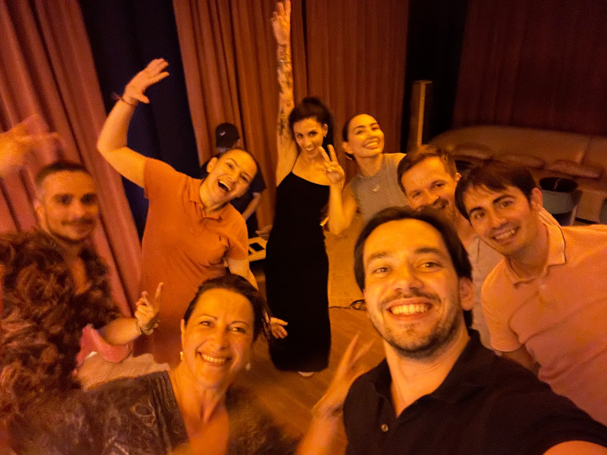 Nine members of the team stand in a circle in a cozy lounge space, smiling and posing.